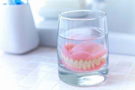 Complete set of dentures in a glass of clear fluid on tiled countertop