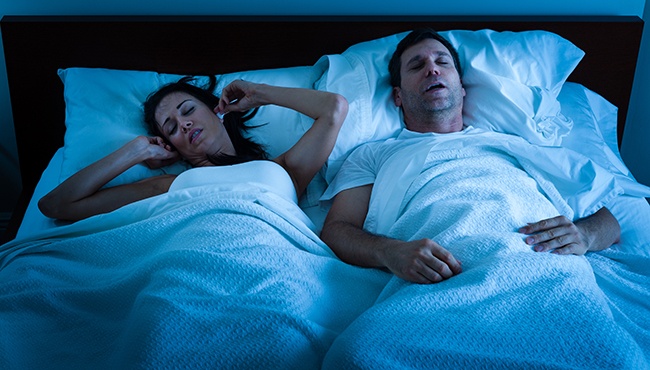 a woman putting ear plugs in to block out snoring sounds from her husband